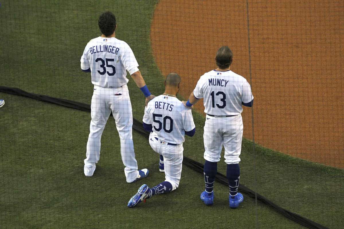 Los Angeles Dodgers' Cody Bellinger, left, and Max Muncy, right, put their hands on Mookie Betts during the national anthem prior to an opening day baseball game Thursday, July 23, 2020, in Los Angeles.