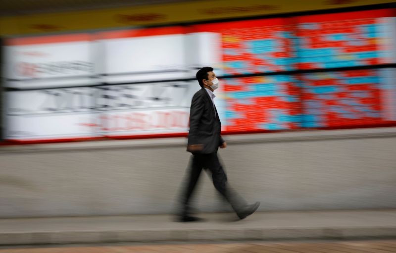 © Reuters. FILE PHOTO: A man wearing a protective face mask, following the coronavirus disease (COVID-19) outbreak, walks in front of a stock quotation board outside a brokerage in Tokyo