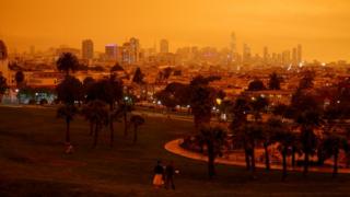 Downtown San Francisco can be seen from Dolores Park under an orange sky