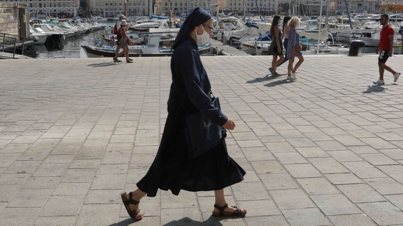 A nun wearing a protective face mask walks at the Old Port in Marseille
