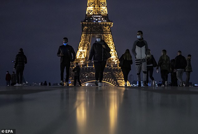 People wearing protective masks walk near the Eiffel Tower hours before the new curfew