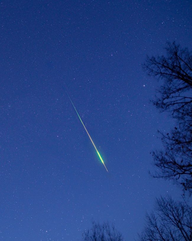 A long and bright colored meteor streak against a bluish sky.