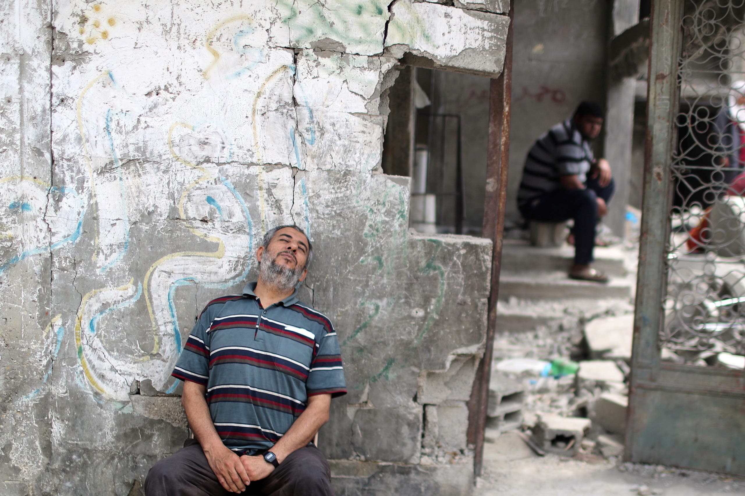 A Palestinian sits beside the rubble of his house in Gaza