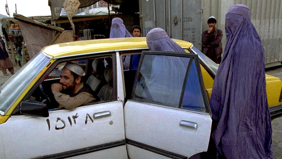Afghanistan: Two women in light blue burqas climb into the back of a white and yellow taxi on a street in Kabul