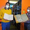 Archive director Johannes Waldschutz (left) and his colleague Christopher Wangenheim display a number of different historical newspapers being digitized.  There are many grapes on the shelves behind them.