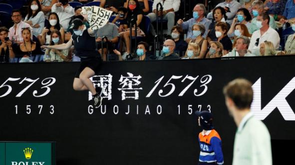 Daniil Medvedev sees exactly what is happening.  The Russian sees the woman jumping from the stands to the field with a sign in her hand