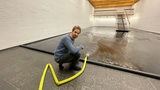 A man sits on the floor and uses a hose to flow water into a room.