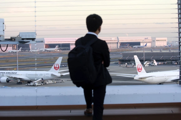 A man looks at a waiting Japan Airlines plane at Tokyo's Haneda International Airport on the 29th of last month.  Station NHK first announced that Japan will suspend new reservations for all incoming flights for a month to contain the new strain of the virus.  Yonhap News Agency 01-12-2021